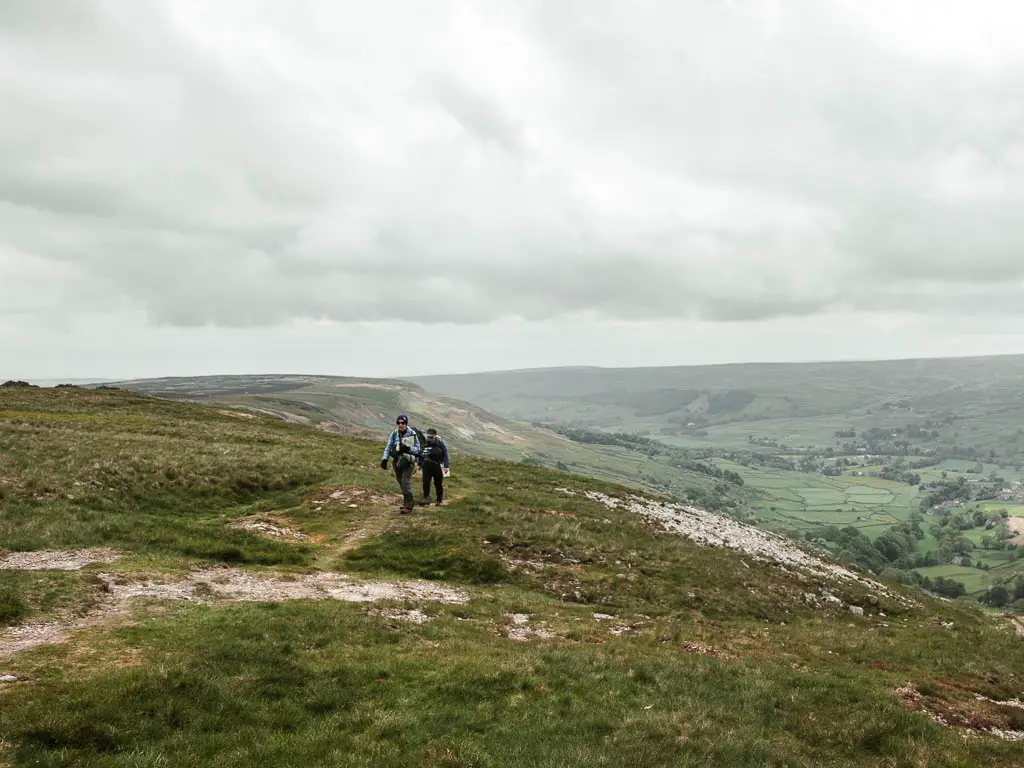 Two people along along the edge of the hill top, with the valley below to the right.