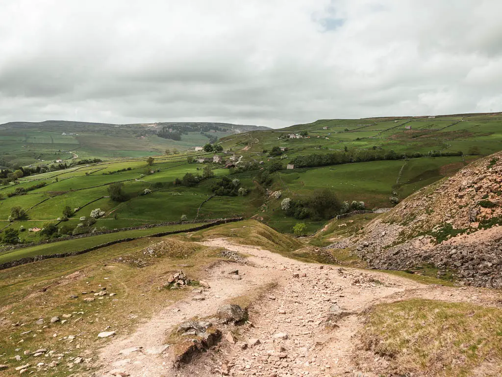 A rocky dirt path with a view to the green hills undulating ahead.