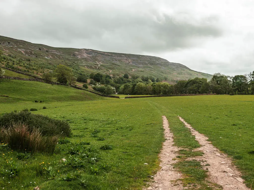 A trail leading straight across a large grass field, with Fremington Edge rising up above to the left.
