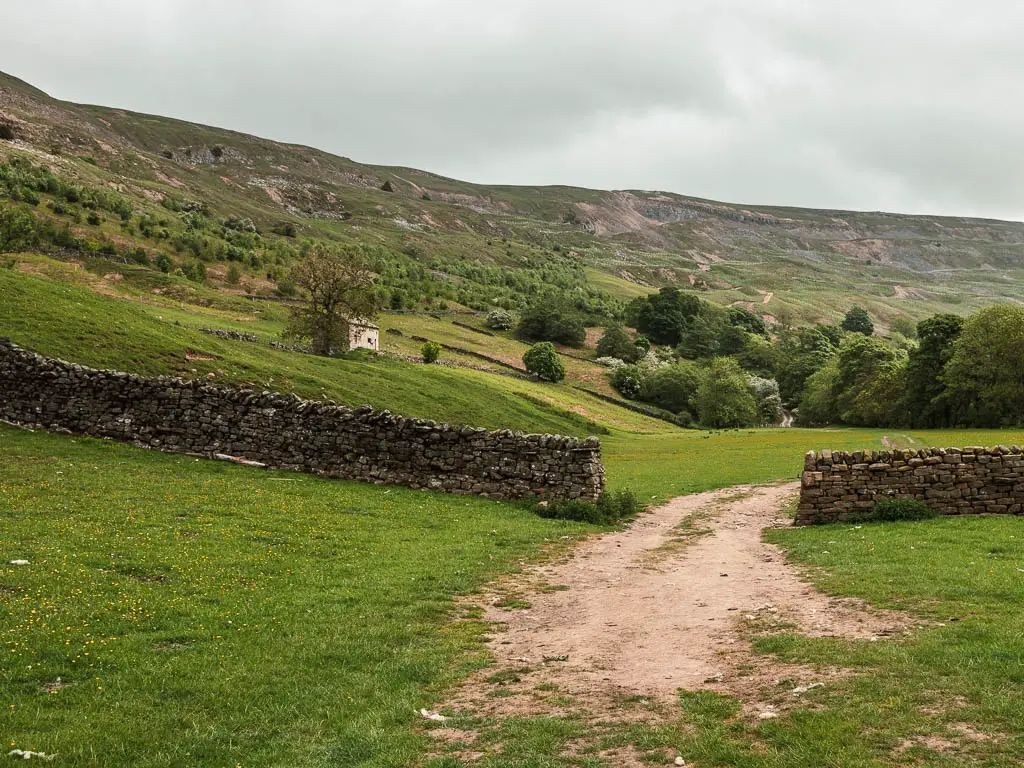 The path leading through an opening in the stone wall, going from one field to another, on the walk though the bottom of the valley, with Fremington Edge rising up to the left.