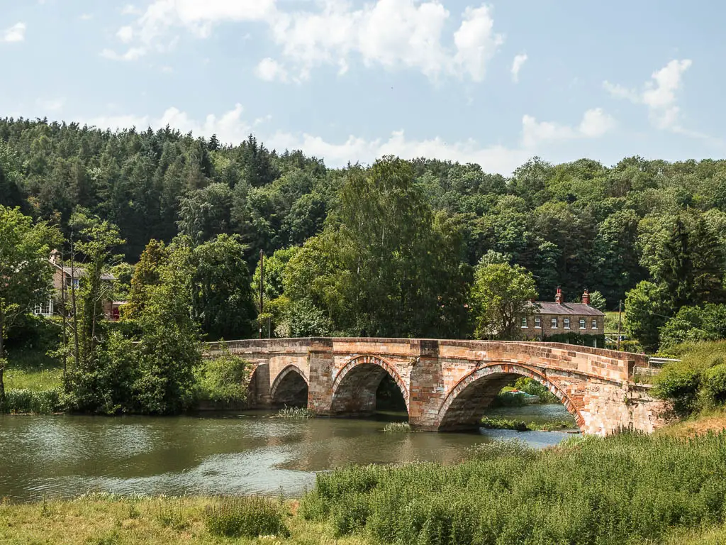 A pretty arched bridge over the river, at the start of the walk at Kirkham Priory. There are lots of green leafed trees on the other side of the river.