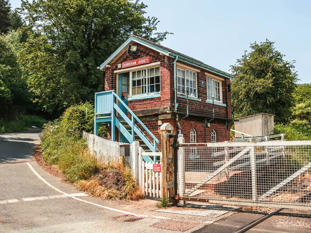 The Kirkham Abbey train station building next to the road. It has brick walls, and light blue steps leading up to the entrance. 