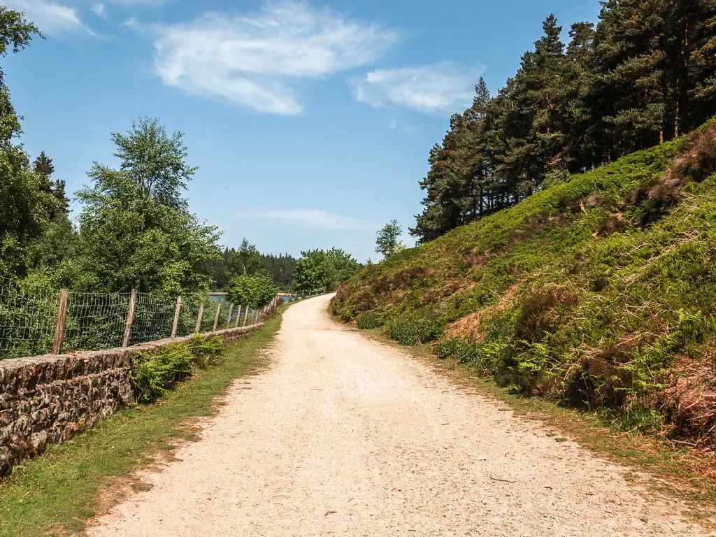 A wide path leading uphill, with a stone wall and wire fence to the left, and green hill up the right side.