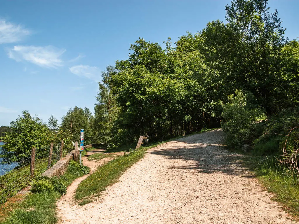 A stoney path leading up towards the green leafy trees to the right, with a small walking trail leading away tor the left.