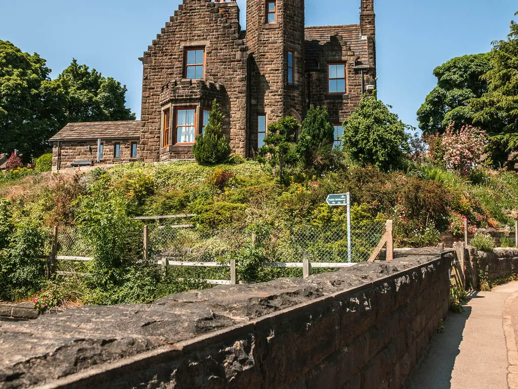 A stone wall, with a trail sign pointing left, ahead, and a stone walled building on the other side.