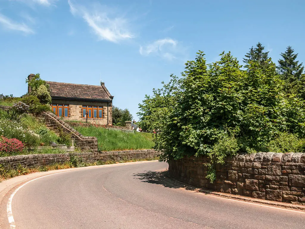 The road as it curves to the right, lined with stone walls, and a cottage ahead.