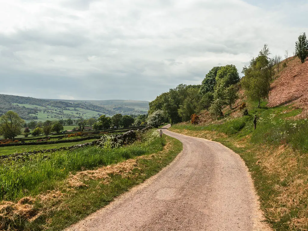 a road curving ahead, with a big hill rising up on the right side, and fields down to the left.