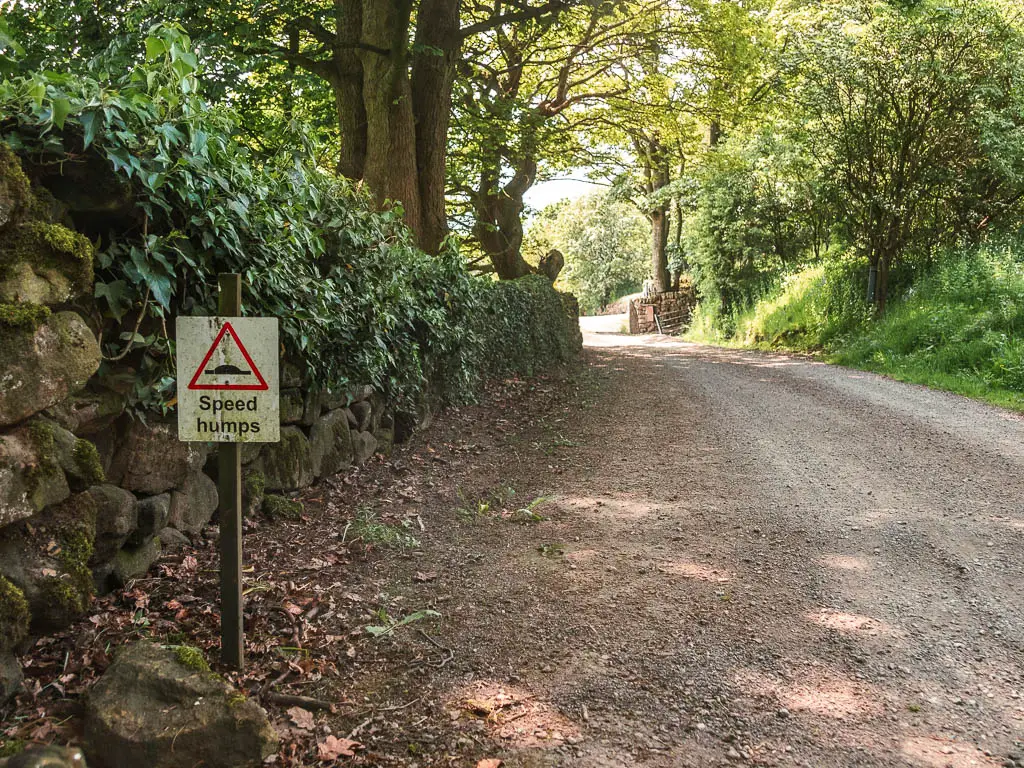 A small sign on the left side of the gravel road saying 'speed humps'. 