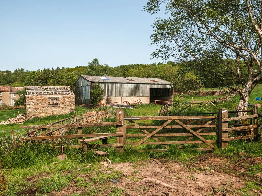 A wooden fence and gate, with farm buildings on the other side.