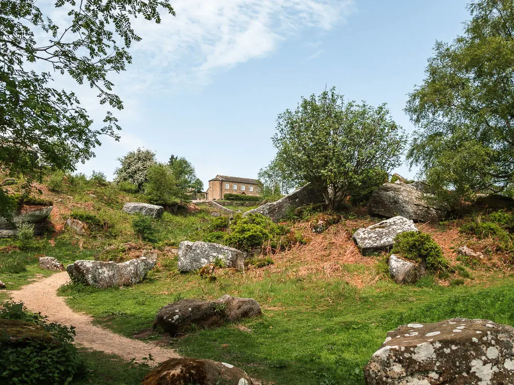 A small green hill with a few smaller rocks, and a house in the distance up a hill.