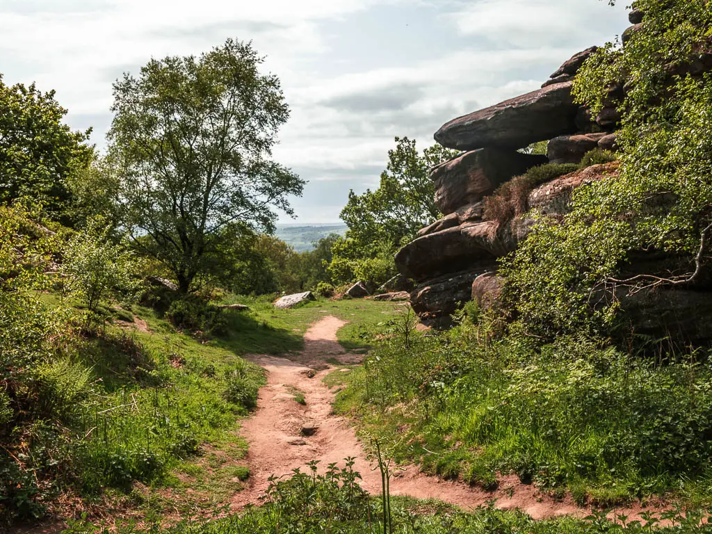 A rugged path with a grass hill on the left, and big rocks to the right, and an opening ahead.