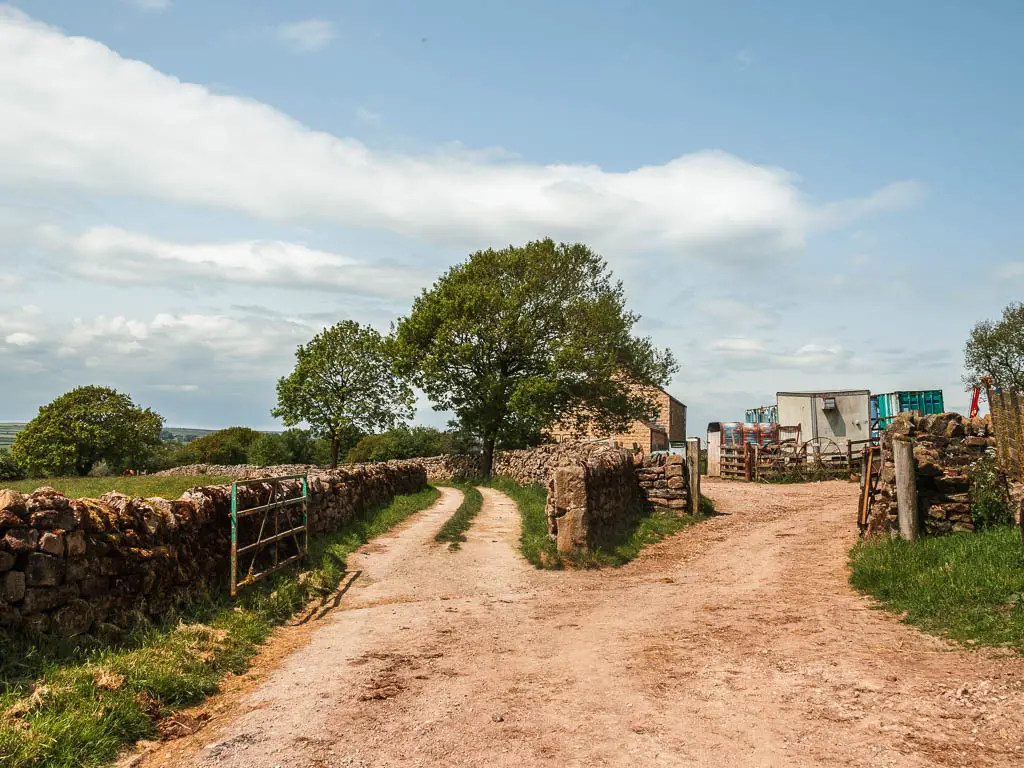 A fork in the dirt road, with the right one leading to a farm, and the left one lined with stone walls.