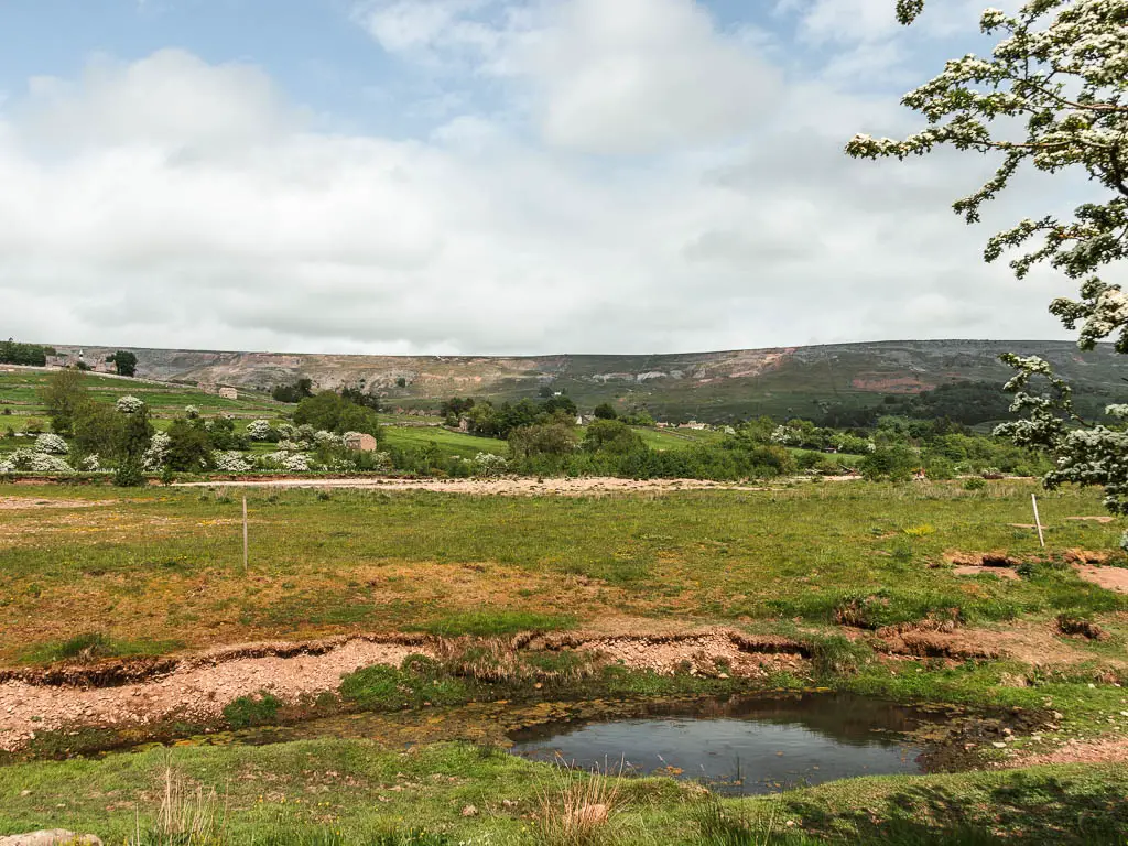 Looking across the large grass fields, with a small pond and a big hill rising up in the distance. 