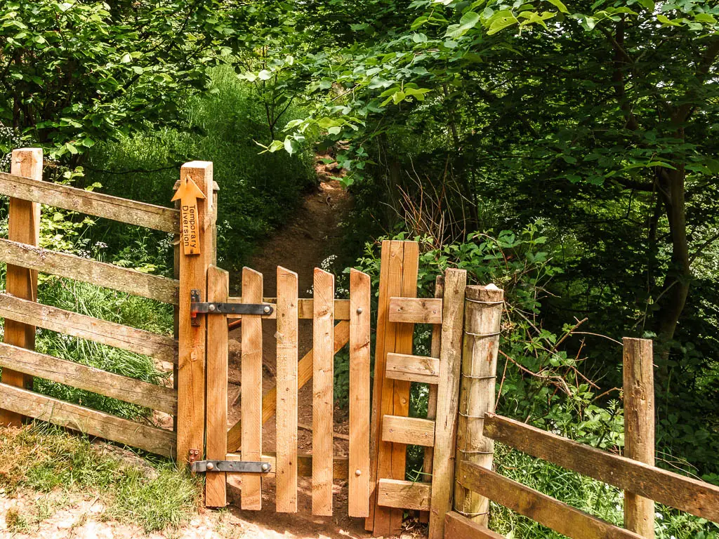 A wooden gate with a dirt trail leading under the trees on the other side.