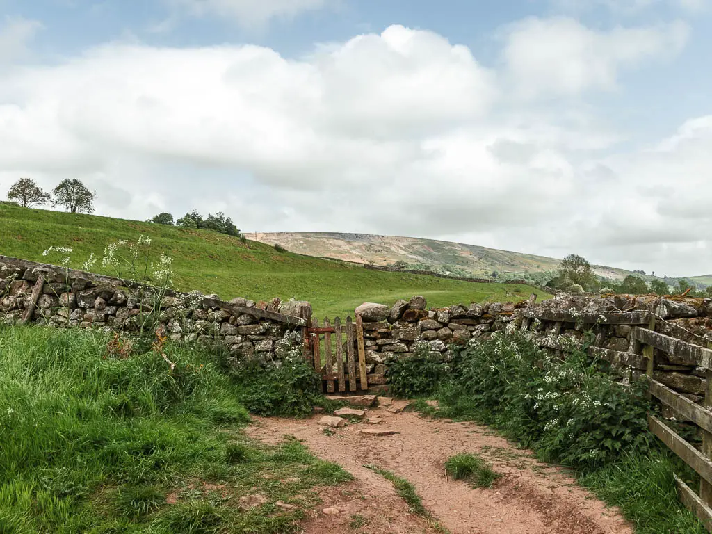 A wooden gate in a stone wall, with a dirt trail leading to it, on the Reeth circular walk.