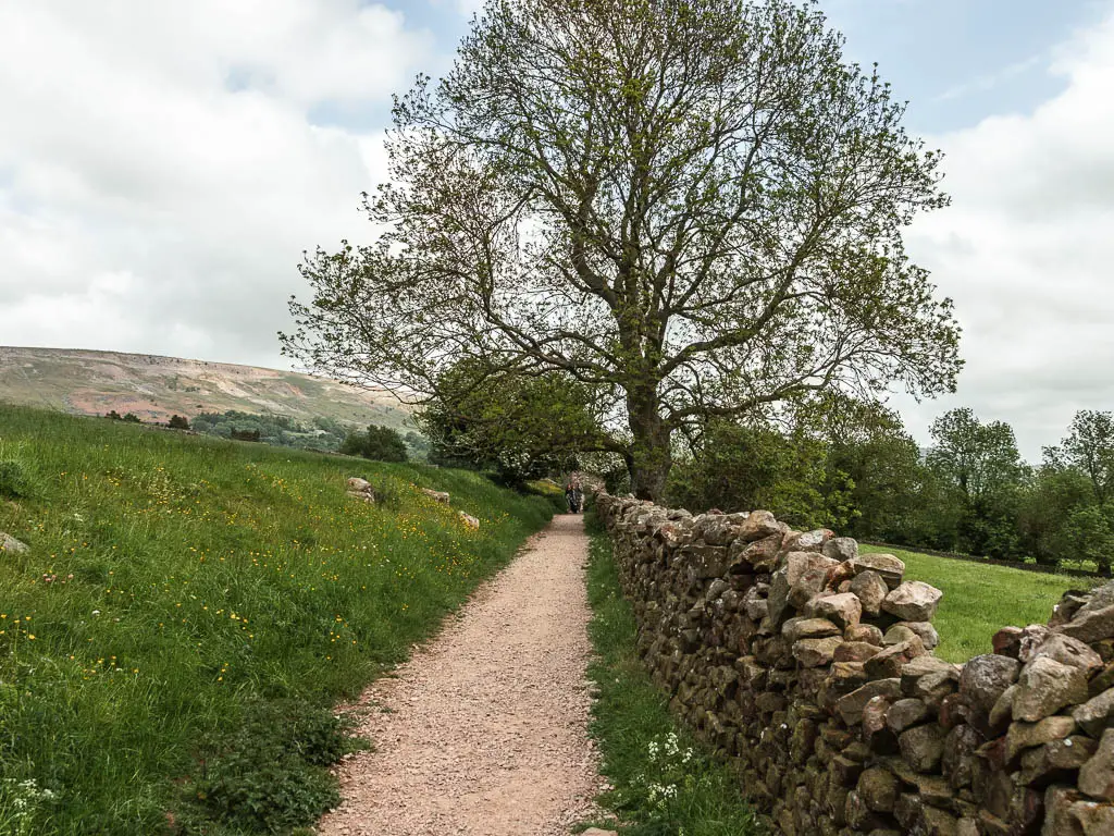 A gravel path with a hill rising up to the left, and a stone wall to the right.