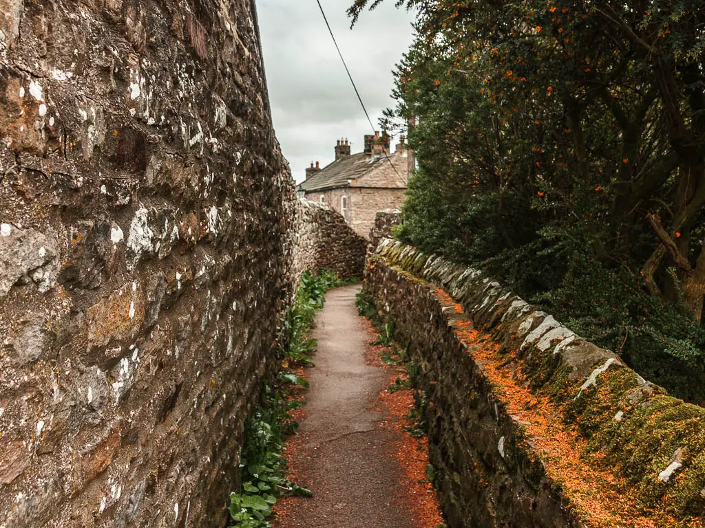 Walking through a gap between the stone walled building on the left, and stone wall on the right.