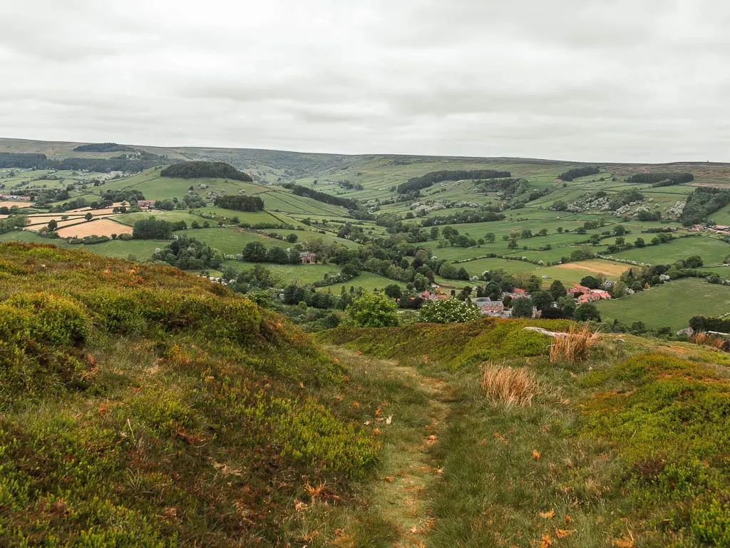  trail leading through a trough in the grass field, with a view to the village of Rosedale Abbey at the bottom of the valley below.