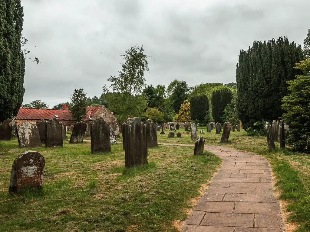 A path leading through a graveyard with headstones on the green to the left.