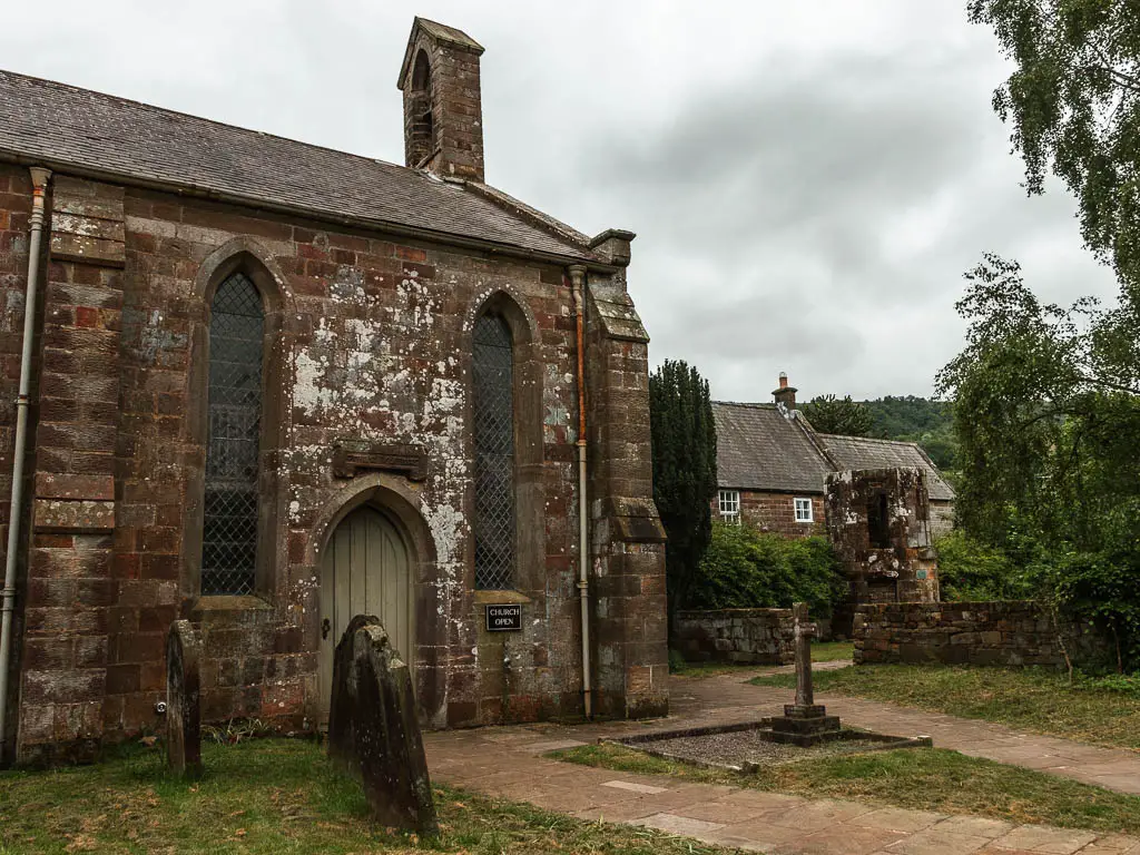 A church to the left, and a path leading around to the right. There are a few gravestones in front of the church.