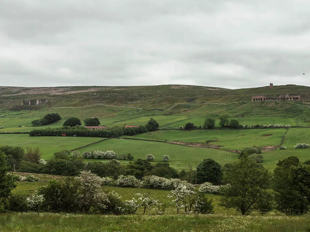 A big hill, with trees dotted about, and some of the industrial mining ruins on the side of the hill, on the walk from Rosedale Abbey.