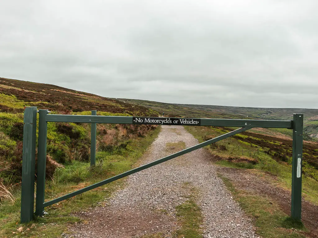 A metal barrier across the gravel path of the Rosedale Railway, on the walk up to Blakey ridge. There is a sign on the barrier saying 'no motorcycles of vehicles'.