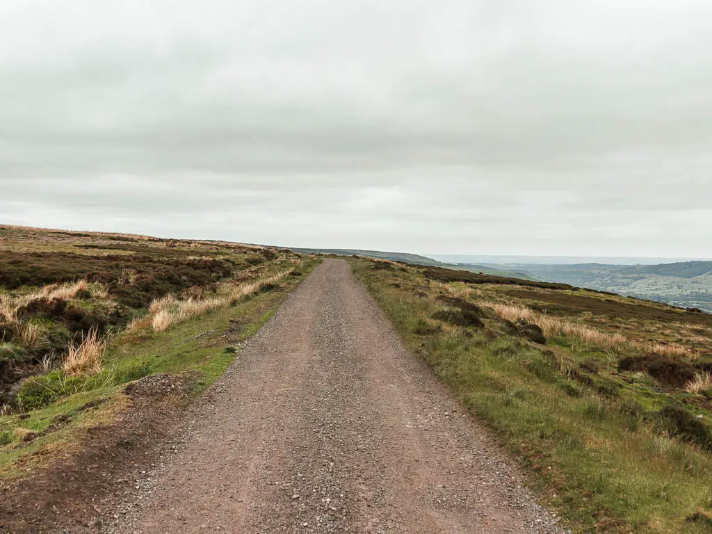 A wide gravel path leading straight, surround by green and brown coloured moorland.