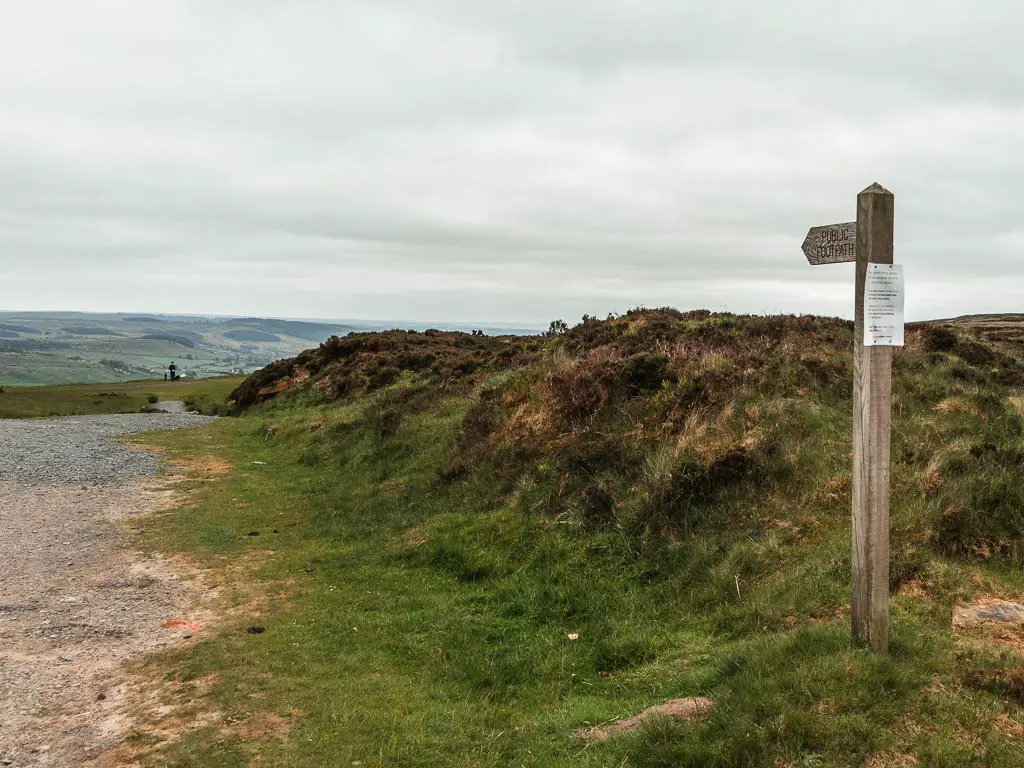 A wooden footpath sign on the green grass patch on the right, with the gravel path to the left.