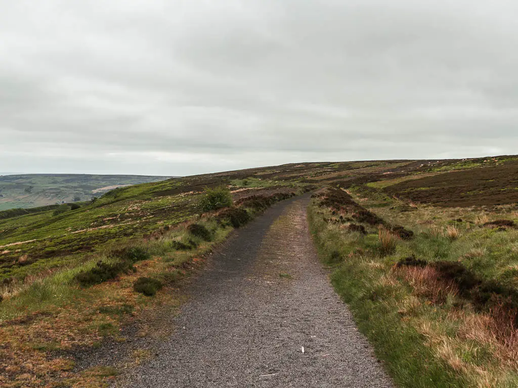 The gravel Rosedale Railway path, lined with grass and brown heather moorland, on the walk back towards Rosedale Abbey.