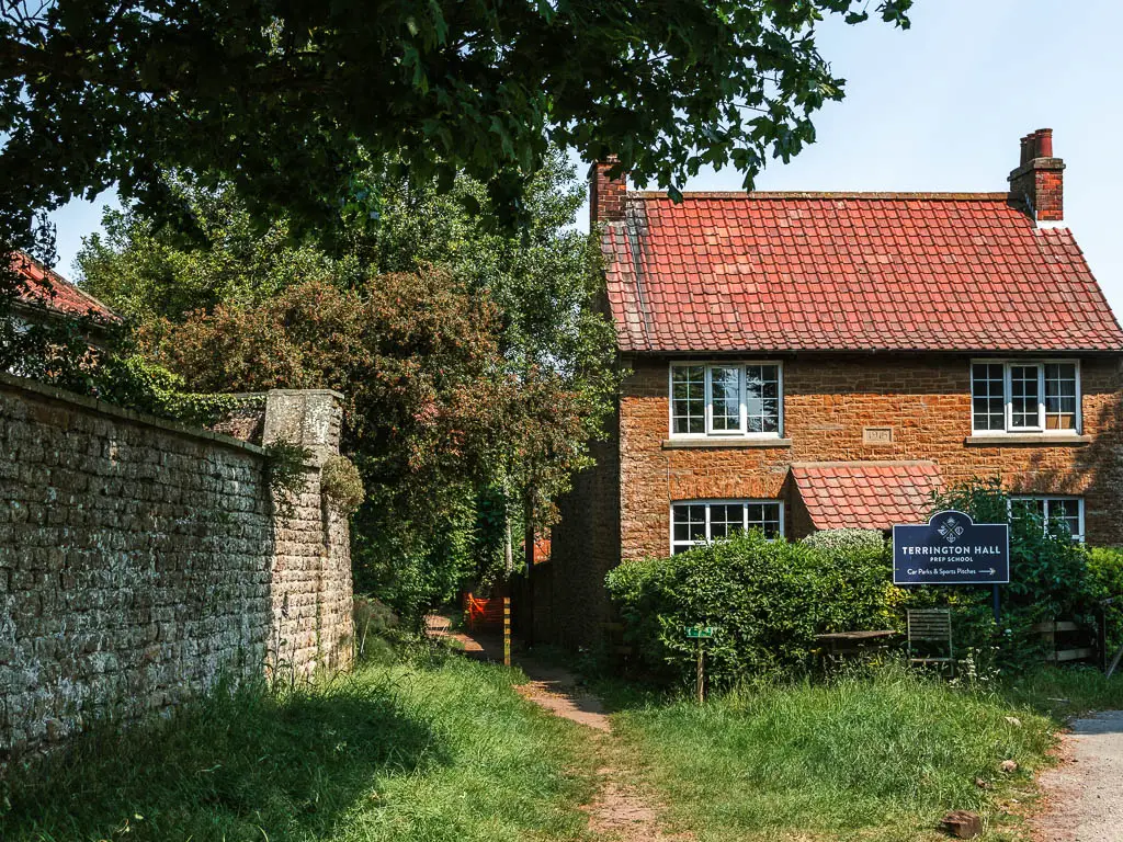 The trail leading between a house and stone wall.