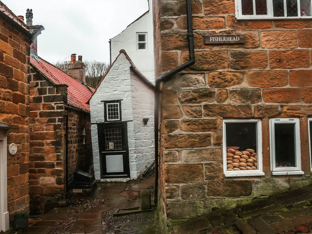 A thin white coloured cottage nestled between the stone buildings in Robin Hood's Bay.
