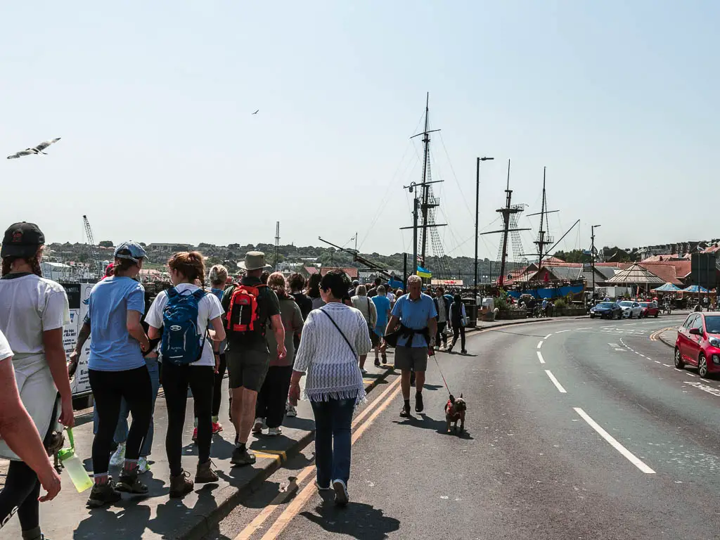 A road with a pavement to the left, and masses of people walking along it.