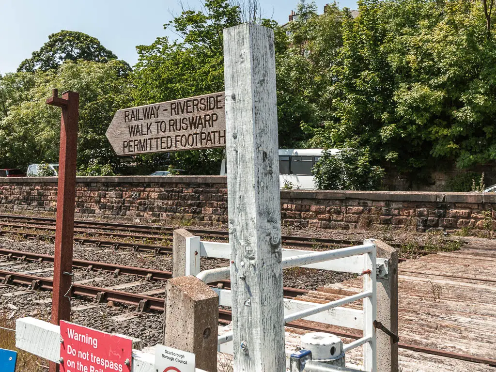 A wooden footpath sign with a railway track behind it.