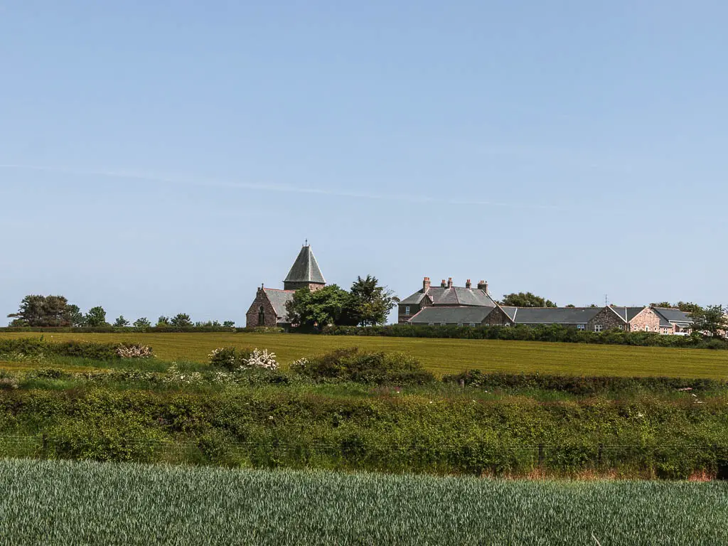 Looking over the green fields, with some rooftops and church ahead on the other side. 