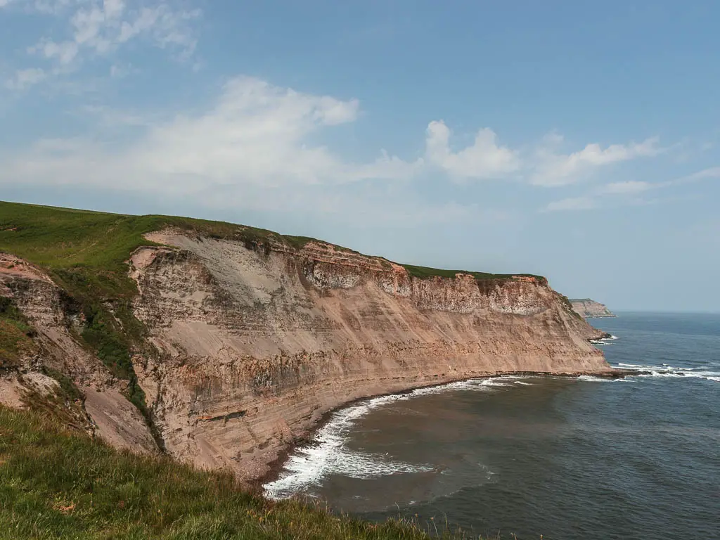 The rocky cliffside curving around, with the dark blue sea below, on the coastal walk from Robin Hood's Bay to Whitby.