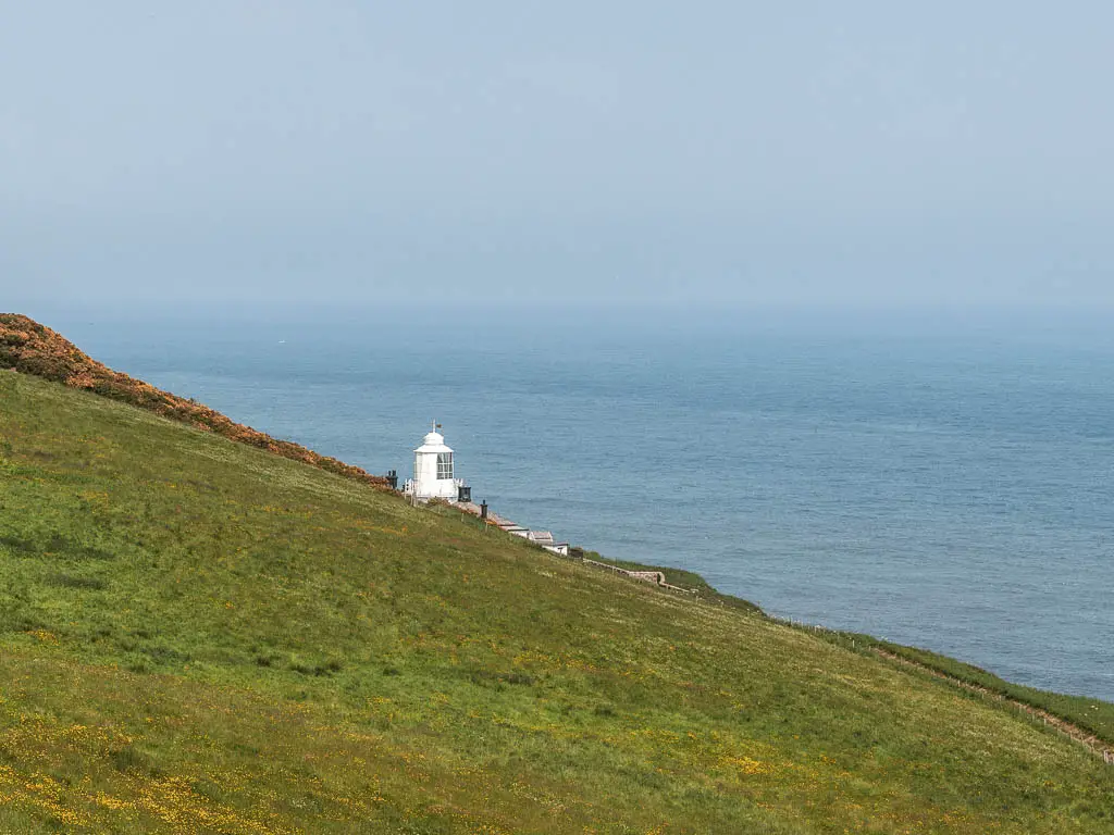 Looking across the green grass hill, to a white lighthouse ahead, and the blue North Sea behind.