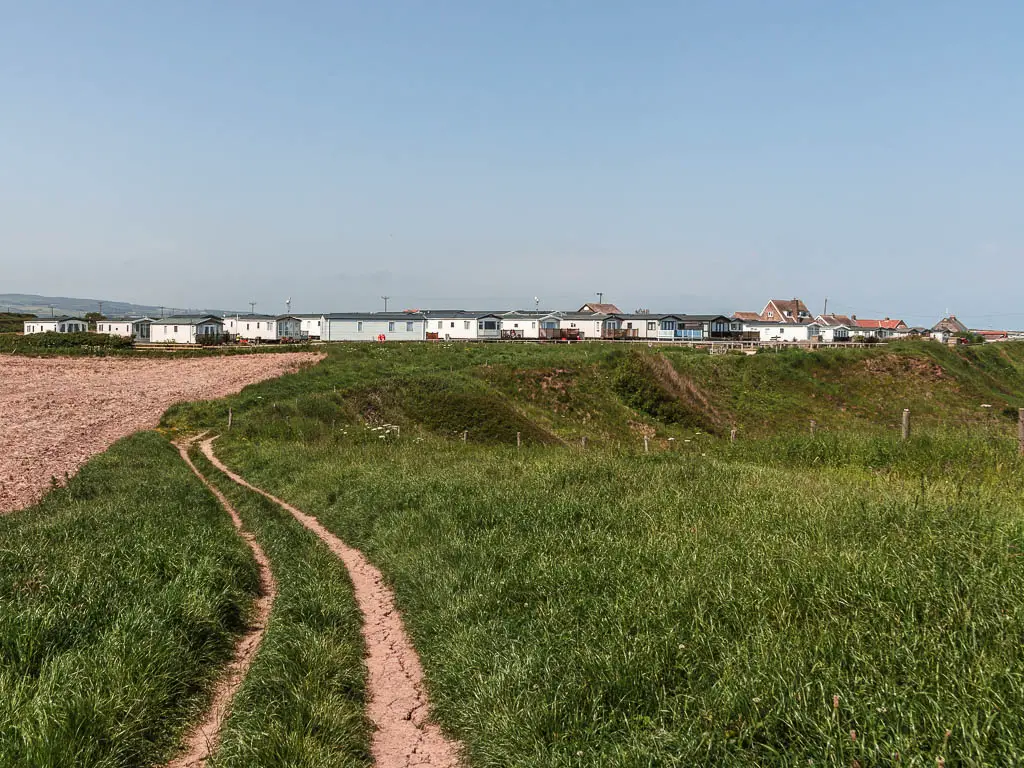 A trail track through the grass, with holiday caravans ahead.