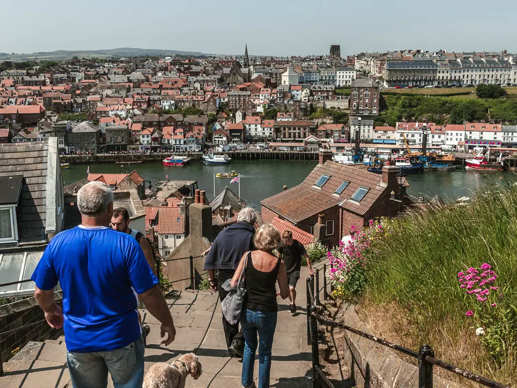 Loots of people walking down the 199 steps, with a view to the rooftops of Whitby below, and the river running though them, after the walk from Robin Hood's Bay.