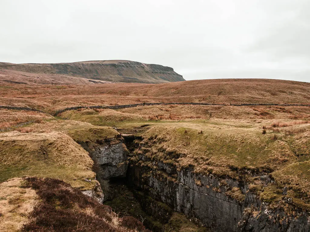 The deep cavern of Hull pot, with a view to Pen-y-Ghent ahead in the distance, on the walk around it, in the Yorkshire Dales National Park.