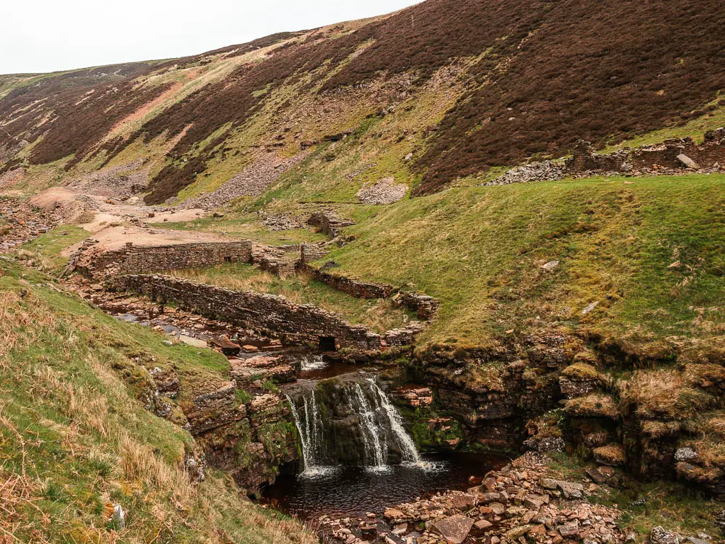 Looking down into the Gunnerside Gill  valley dip, part way through the walk through the Swaledale area of the Yorkshire Dales. There is a waterfall dropping into a pool of water at the bottom.