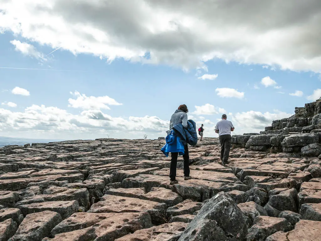 People walking along the rocks with gaps at Malham Cove, in the Yorkshire Dales National Park.