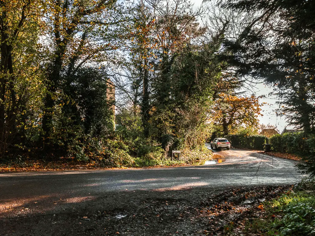 A road running from left to right and then curving straight, with green leafy trees and bushes in the curve on the other side.