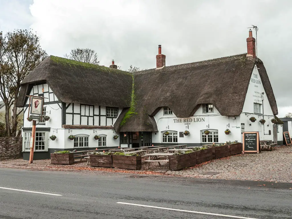 Looking across the road to the red lion pub in Avebury. The pub as white walls and a thatched roof.