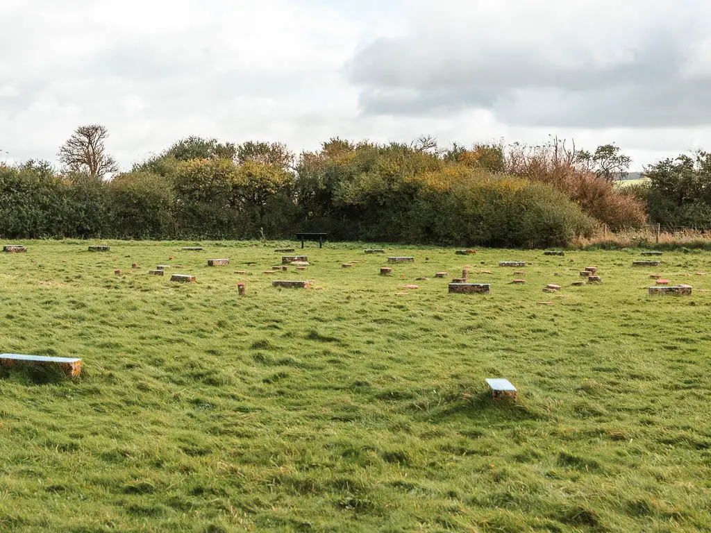 A large green grass field with small concrete blocks scattered about in the Sanctuary, when walking between Avebury and Ogbourne St George. There are trees on the other side of the field.