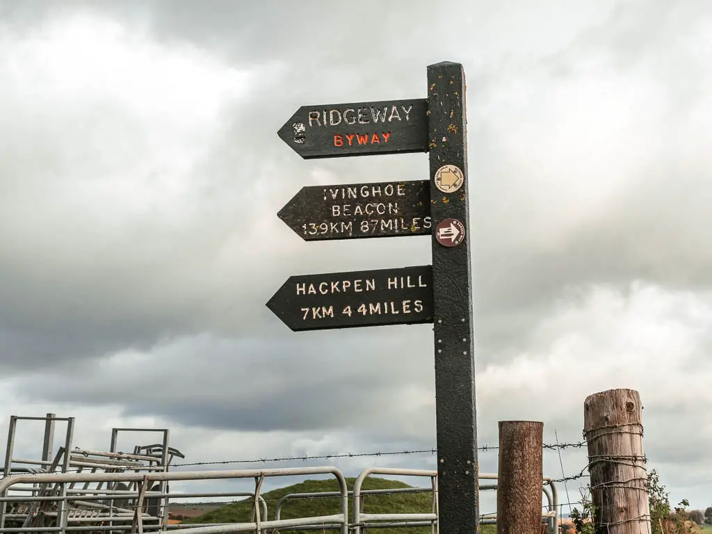 A black wooden trail sign post, pointing left to walk along the Ridgeway, between Avebury and Ogbourne St George.