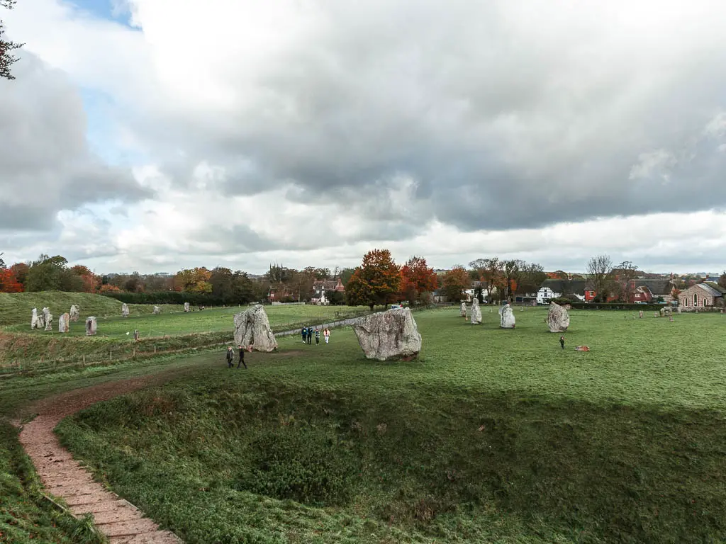 Looking down across the large field, with lots of big stones dotted about in Avebury. There are a few people walking in the field.