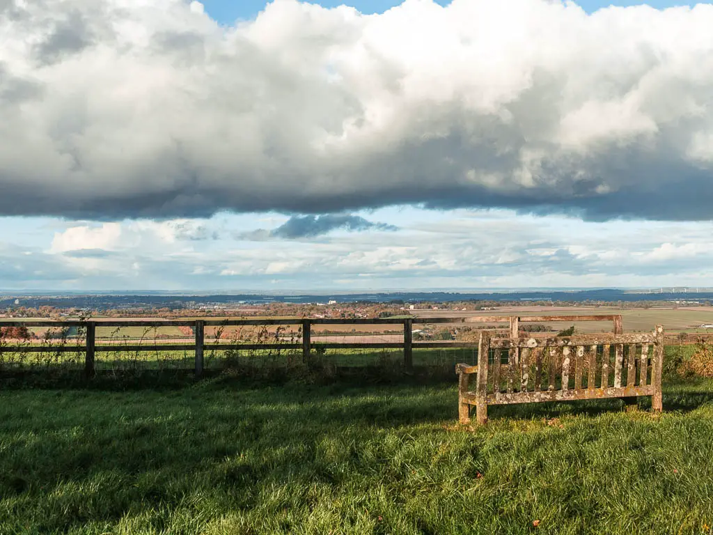 A wooden bench facing a view of fields as far as the eye can see.