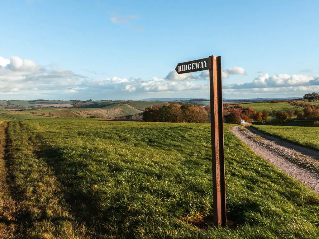 A metal trail sign saying 'ridgeway' pointing across the field, near the end of the walk from Avebury to Ogbourne St George.