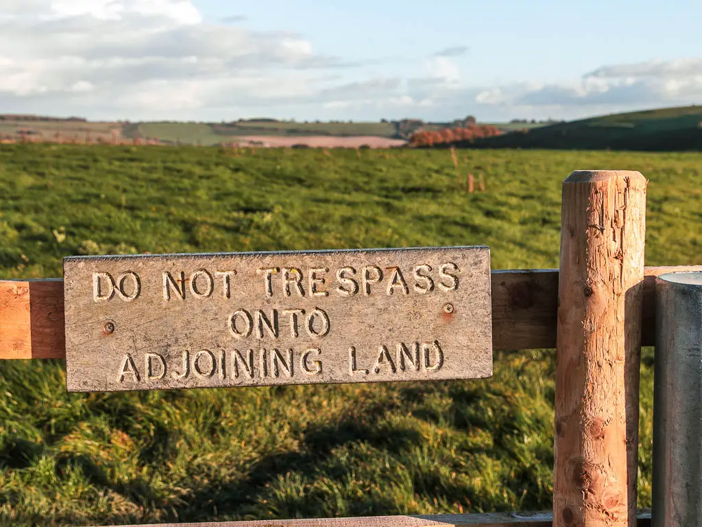 A sign in front of a large grass field saying 'do not tress pass onto the adjoining land'.