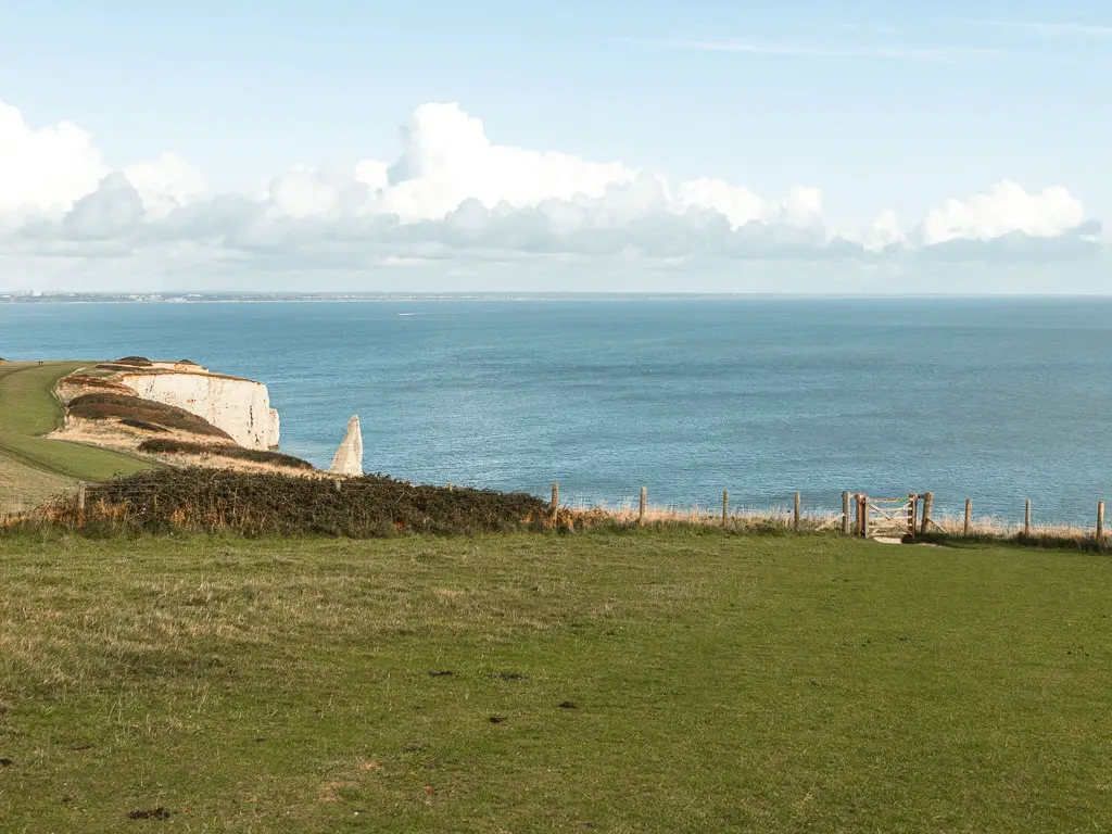 Walking across the field of Ballard down with a gate and fence ahead, and the white cliffs leading into the sea.